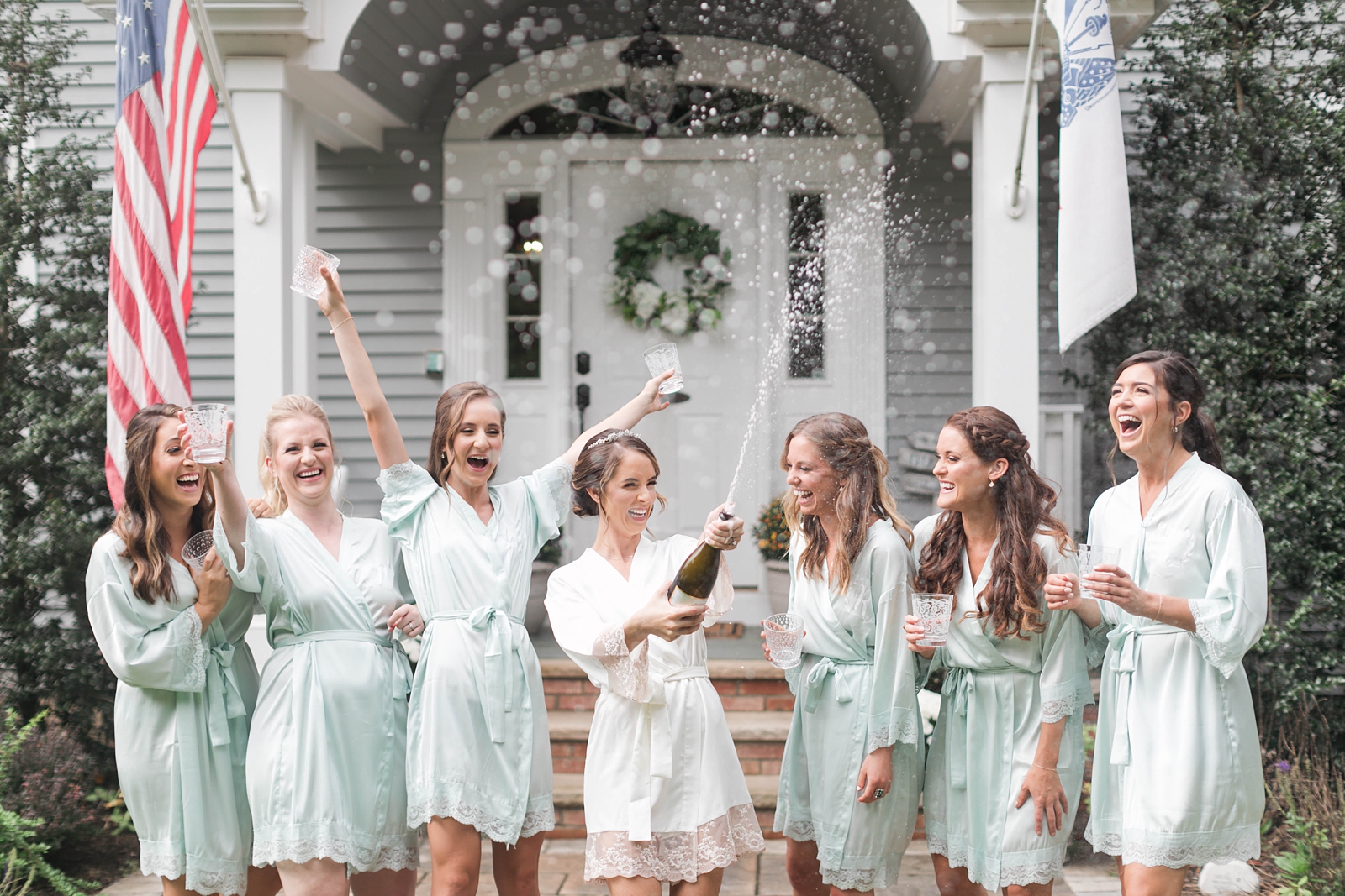 bride and bridesmaids pop champagne on wedding day wearing light green robes