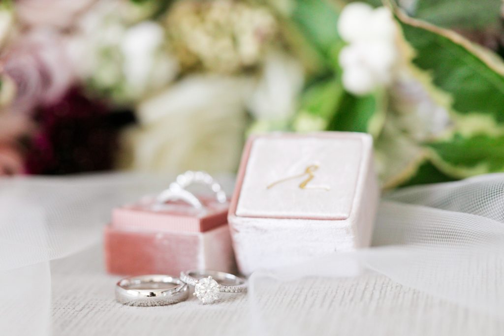 blush ring box and silver wedding rings in front of brides bouquet