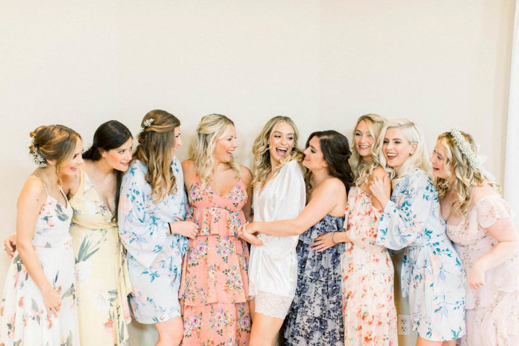 bridesmaids in their floral dresses hug on bride before getting ready